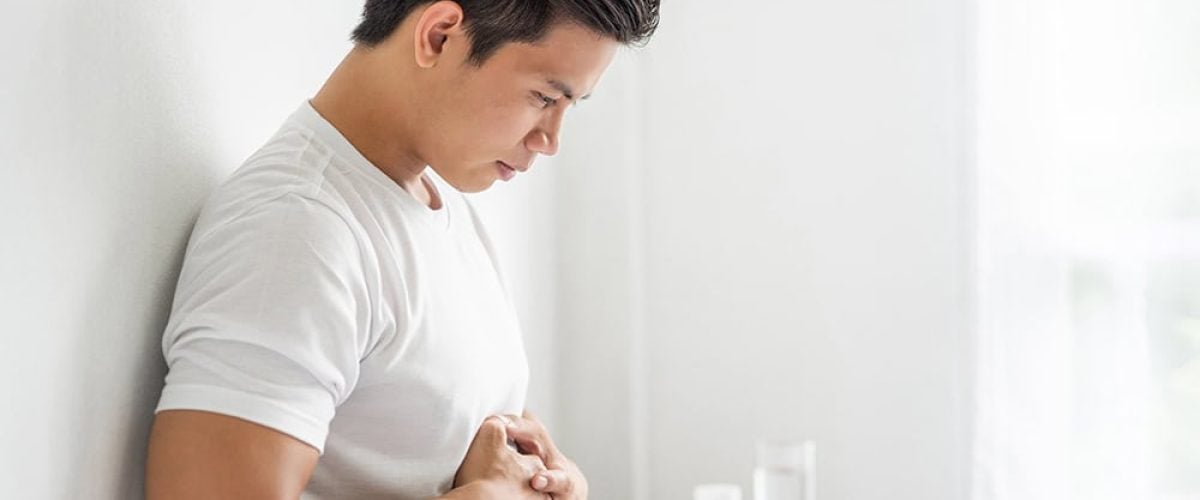 A man sits in bed with a stomachache and presses his stomach with his hands.